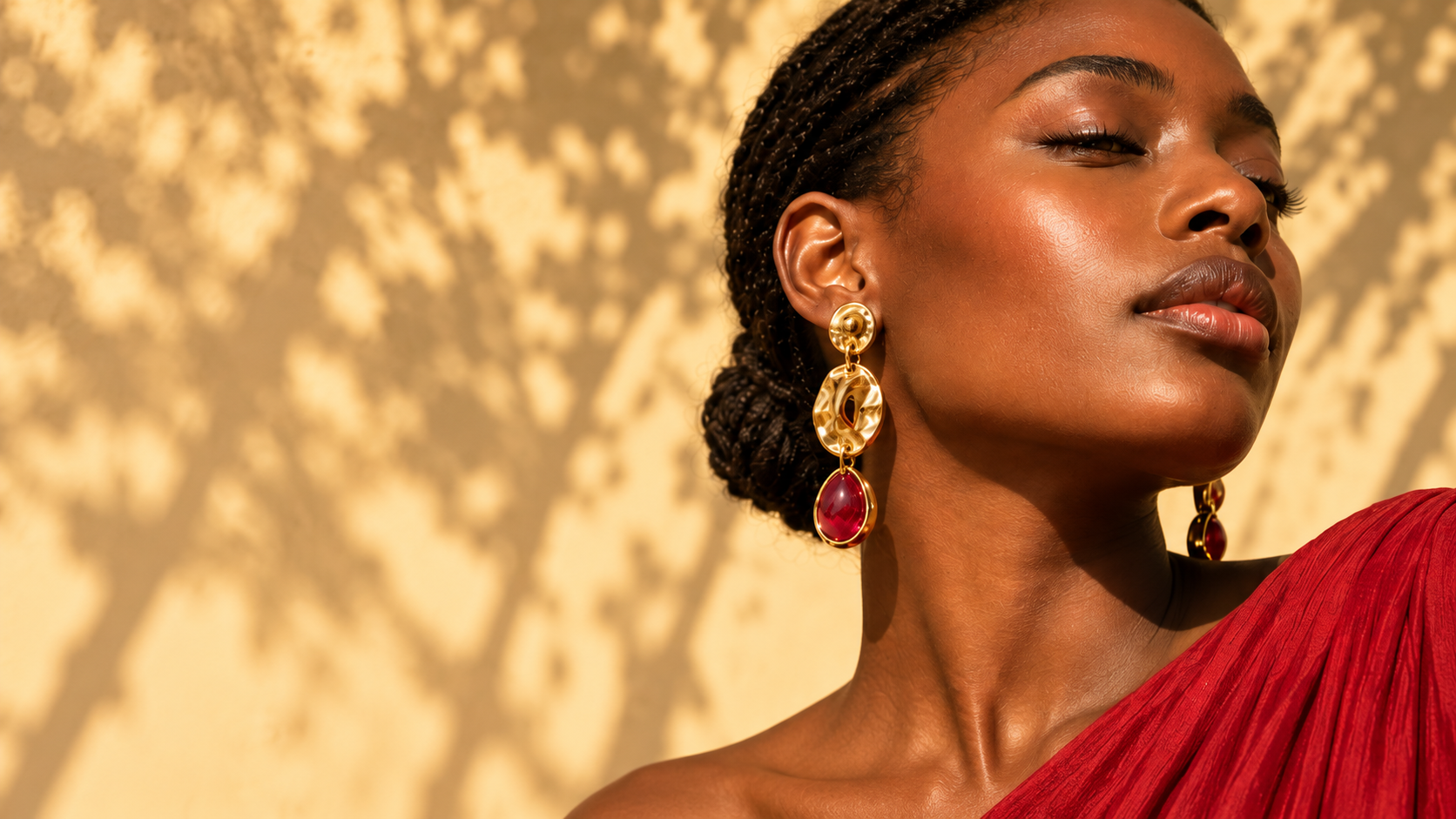 Woman in warm sunlight wearing sculptural gold earrings with ruby drops